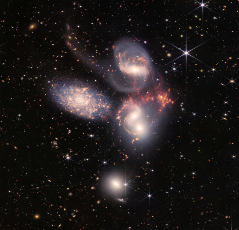 A group of five galaxies that appear close to each other in the sky: two in the middle, one toward the top, one to the upper left, and one toward the bottom are seen in a mosaic or composite of near and mid-infrared data from NASA's James Webb Space Telescope, a revolutionary apparatus designed to peer through the cosmos to the dawn of the universe and released on Tuesday.